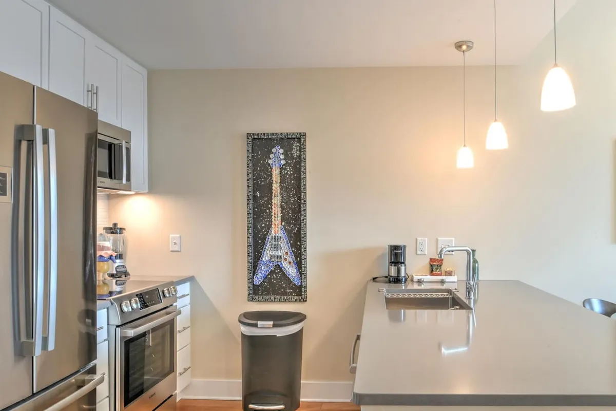 A modern kitchen space with stainless steel appliances, a central kitchen island, and vibrant guitar artwork on the wall. The open layout suggests an inviting atmosphere for both work and social moments, with direct access to the rest of the living space.