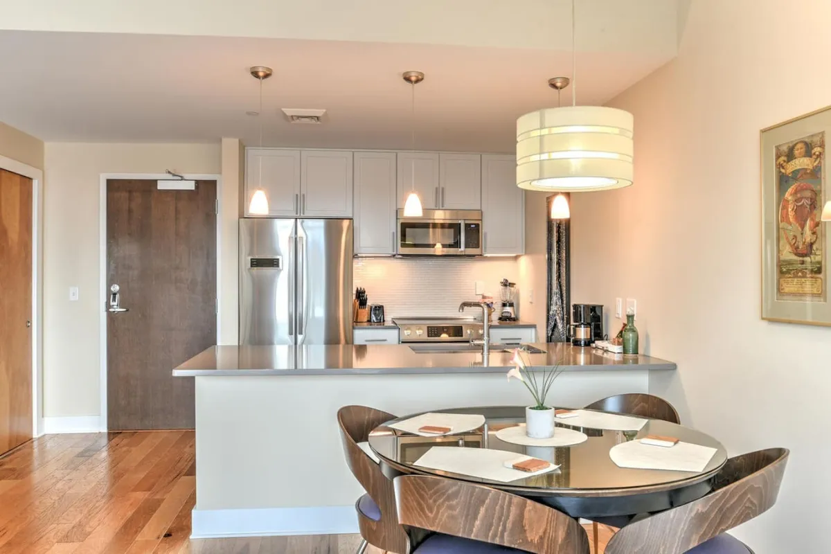 A contemporary kitchen with modern appliances, a round dining table, and stylish wall art. The setting is bright and inviting, perfectly suited for preparing meals or sharing a quiet coffee in the morning.