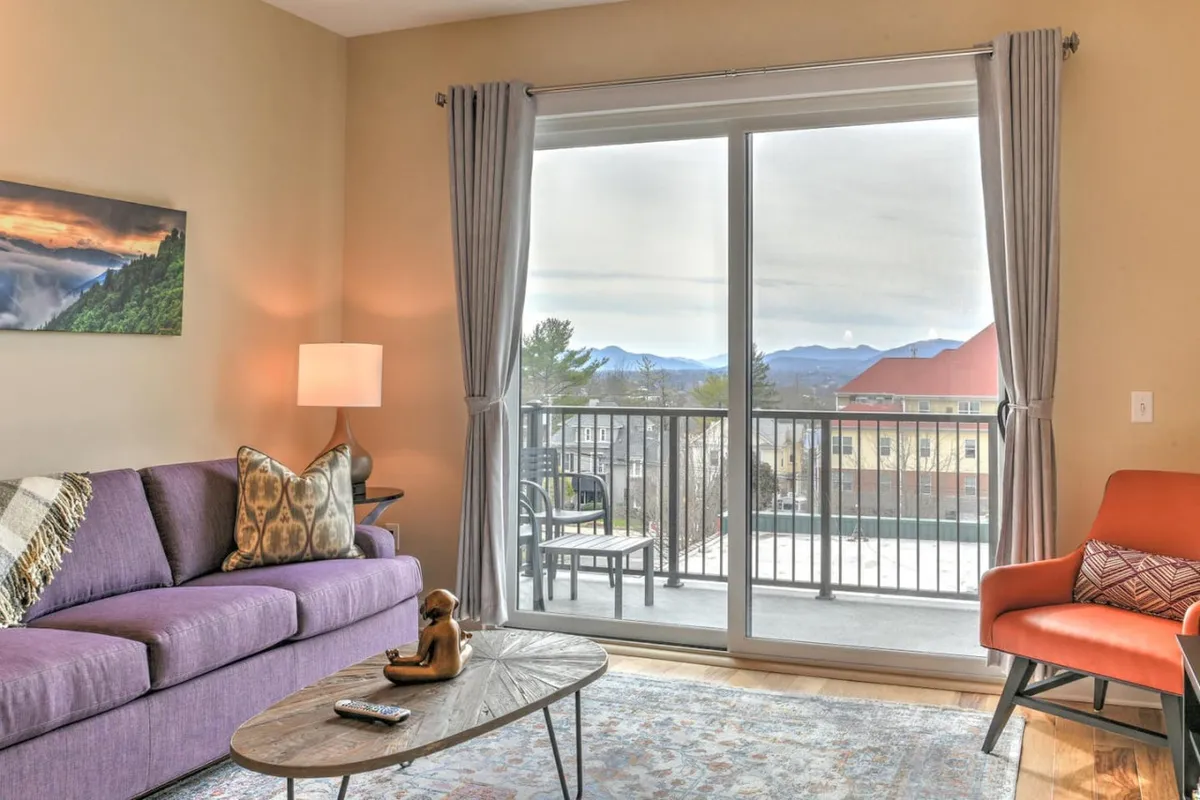 A tranquil corner of the condo’s living room, featuring a large window with mountain views, a round coffee table, and a cozy accent chair. The arrangement allows for intimate moments, with plenty of space for a pet to lounge or play nearby.