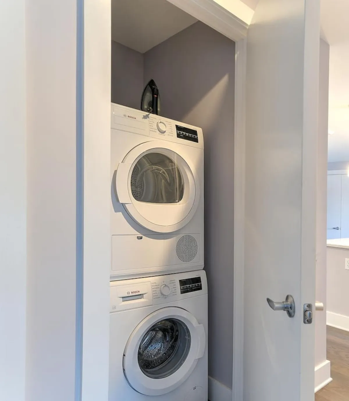 This image features a stacked washer and dryer with an iron on top, situated in a tidy, organized laundry area. The efficient setup suggests a modern building with thoughtful amenities for convenience.