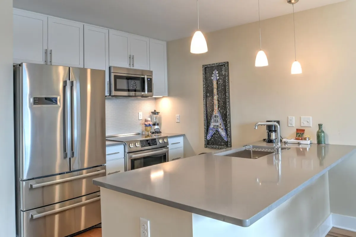 A bright interior kitchen scene featuring stainless steel appliances, a kitchen island, and cheerful Eiffel Tower artwork. The space is lively and well-lit, suggesting an uplifting environment ideal for both quick breakfasts and unwinding after exploring the city.