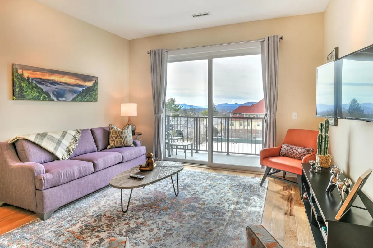 A comfortable interior view of the living space, featuring a large window that lets in natural light, a plush purple sofa, and tasteful decorative art. The ambience is peaceful and bright, providing a sense of security and tranquility for both people and pets.