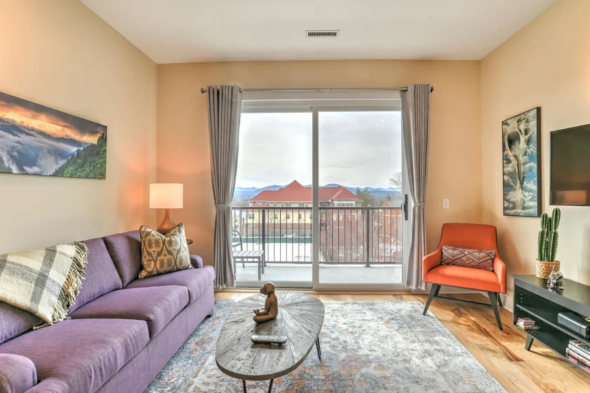 This image showcases a cozy living area featuring a purple sofa, a coffee table, an accent chair, and a beautiful view through the window. The room is spacious and inviting, with ample floor space where a pet could comfortably curl up. The atmosphere is relaxed and homey, ideal for both guests and their furry companions.