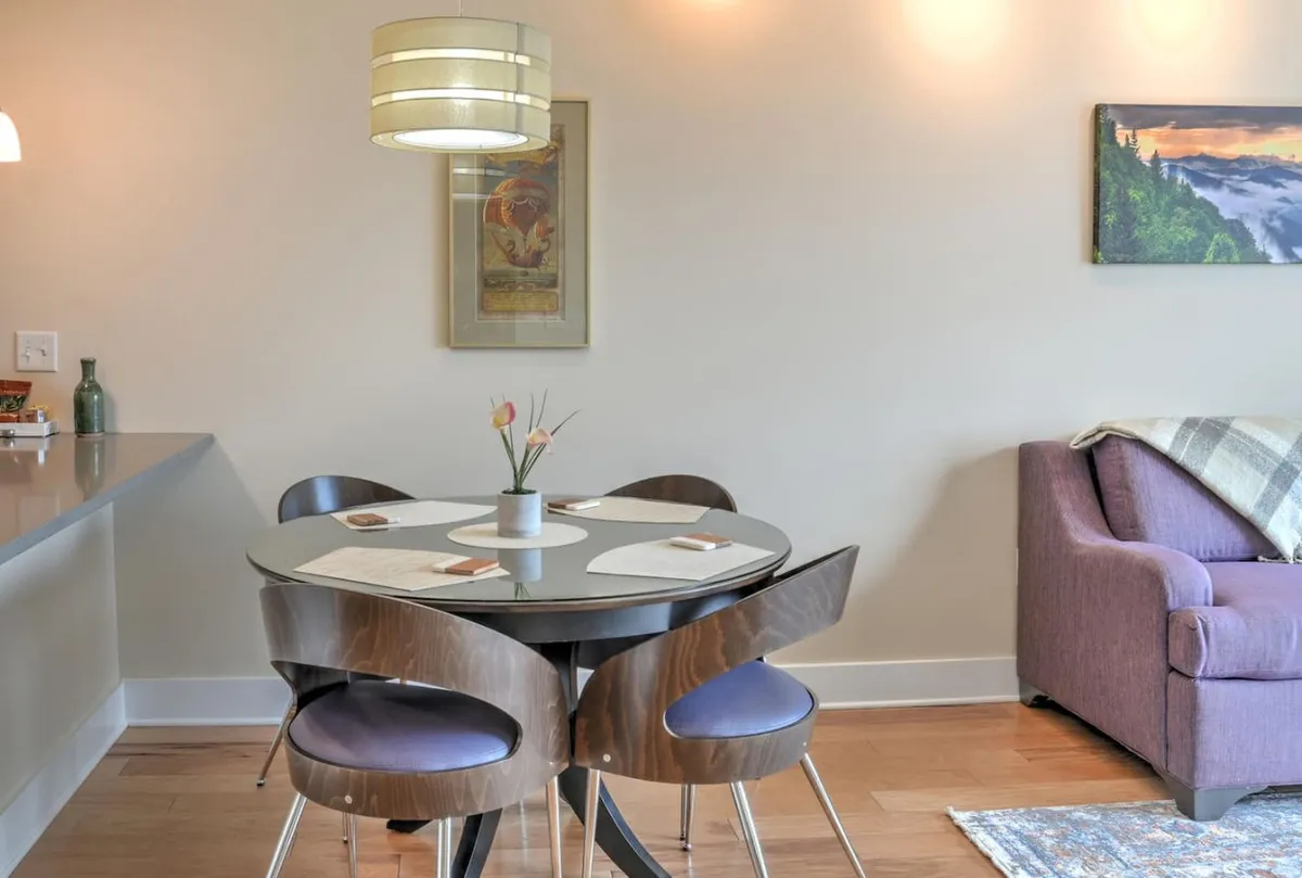 A welcoming interior view of the condo features a dining table with flowers, a comfortable sofa, and artwork on the wall, embodying a cozy, inviting atmosphere for dining, relaxing, and socializing.